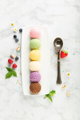 Set of various ice cream scoops and ingredients on white marble background, top view