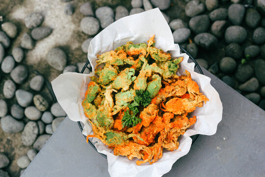 Crispy baby crab with Indonesian balado flavor, topped with leaf garnish and orange and green balado seasoning powder served on a white paper mat in a small black basket. Small crabs for snack.