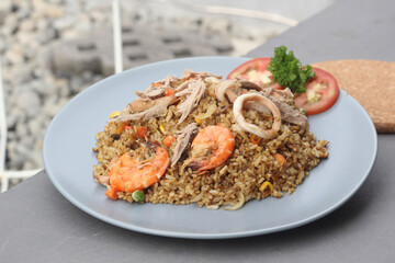 Seafood fried rice topped with squid and prawns served on a baby blue plate with a gray background.