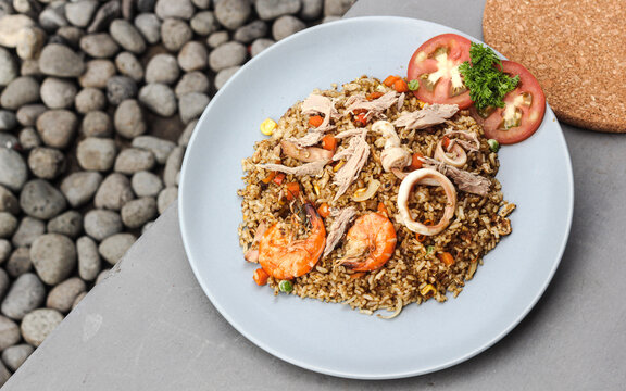 Seafood fried rice topped with squid and prawns served on a baby blue plate with a gray background.