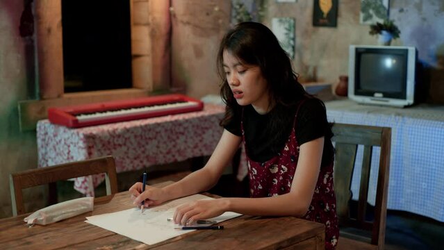 An Asian woman sketching on her drawing book at home space