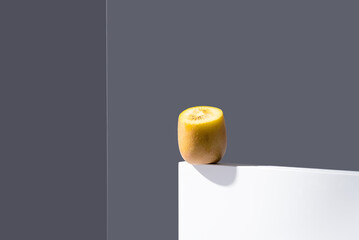 Kiwi amarillo sobre un soporte blanco y fondo gris
