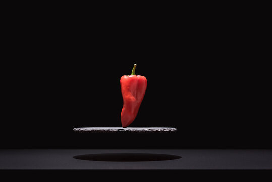 Pimiento rojo fresco suspendido sobre un plato de pizarra y fondo negro	