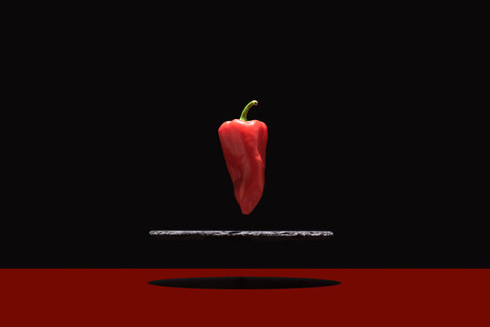 Pimiento rojo fresco suspendido sobre un plato de pizarra y fondo negro	