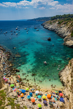 The amazing bay of Porto Miggiano, in Santa Cesarea Terme, resort of Salento, Puglia, Italy. Full of tourists and boats, in the clear, blue and turquoise sea. Small beach enclosed between high cliffs