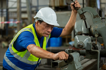 Elderly male worker wear hardhat working at machine in factory. Man technician control metalwork lathe industrial. work factory industrial concept.