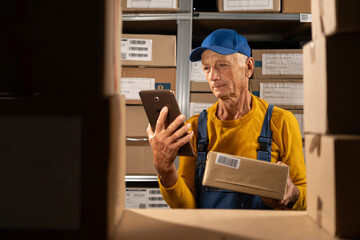 Elderly male warehouse worker uses digital tablet for checking stock