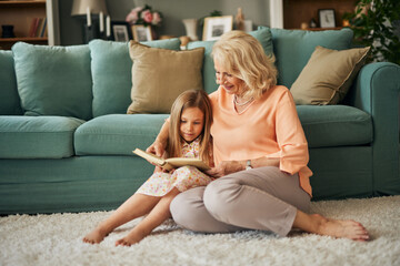Grandma and granddaughter reading a book at home