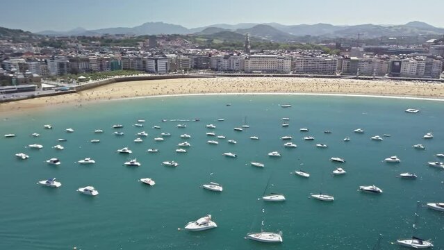 Yachts and boats scattered across the beautiful blue water of La Concha Bay in San Sebastian, Spain.  Golden Ondarreta Beach in the background.