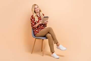 Full length photo of charming cheerful person sit chair hold use tablet isolated on beige color...