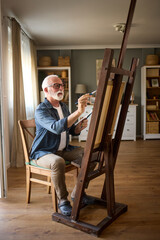 Elderly man painting on a canvas at home