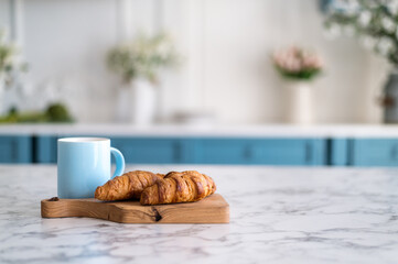 Wooden kitchen board with croissants and blue mug with coffee