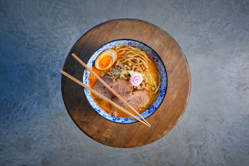 Obraz na płótnie Canvas Chopsticks on bowl of Asian noodle soup served on wooden tray
