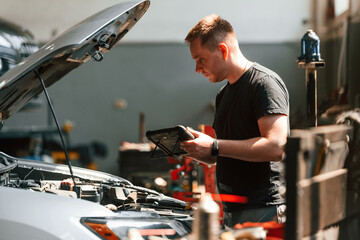 Using the tablet. Man is works in the automobile repairing salon