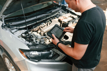 Holding the tablet. Man is works in the automobile repairing salon