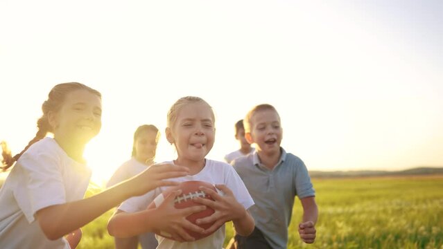 a group of children run on the grass in the park with a ball. happy family childhood dream concept. children lifestyle run on the green grass and play american football together. kids have fun