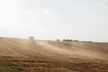 A modern tractor with a heavy trailed disc harrow plows a wheat field at sunset.