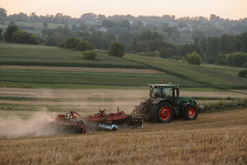 Fototapeta premium A tractor plows a wheat field. The concept of the work of a farmer and harvest.