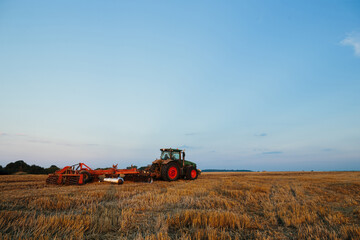 Modern tractor with a heavy trailed disc harrow works a wide hilly field. Autumn or spring agricultural campaign