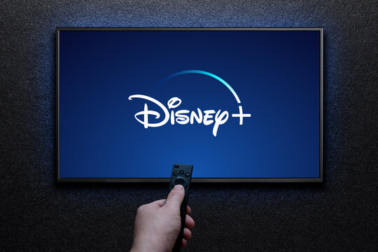 Disney plus logo on TV screen. Man turns on TV with remote control. Disney plus is an American subscription video streaming service. Astana, Kazakhstan - July 21, 2023.