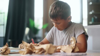Portrait of exhausted school boy with failed crumped papers while writing in notebook at home Tired little kid child with creative block or lack of inspiration indoors Stress education concept