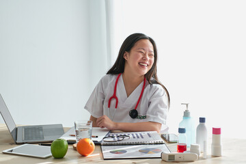 Smiling Asian doctor working at table in hospital