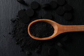 Activated charcoal powder in a wooden spoon on a dark background