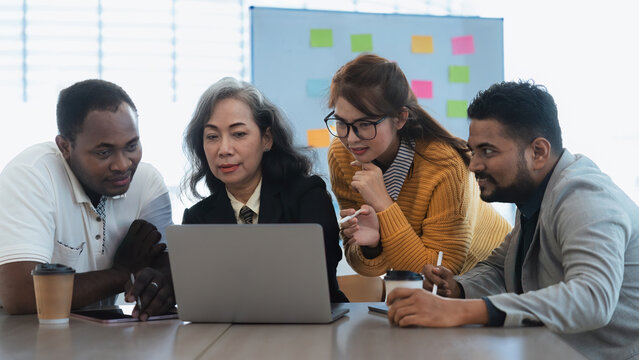 Happy senior old korean businesswoman discussing statistics concept on laptop with african american indian and asian male colleague working together workplace, analyzing electronic documents - Powered by Adobe