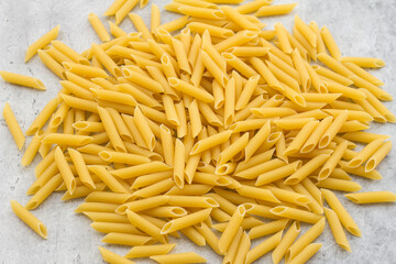 Dry penne pasta on gray textured background, top view