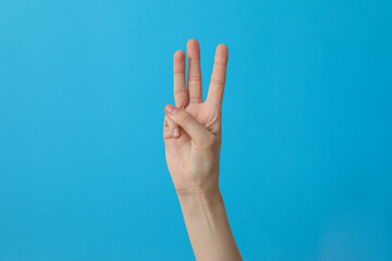 Female hand showing three fingers on a blue background