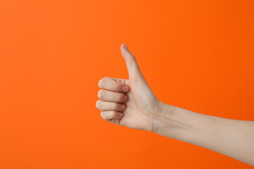 Female hand showing thumb up on orange background