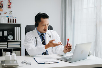 Attractive male doctor talking while explaining medical treatment to patient through a video call with laptop in office