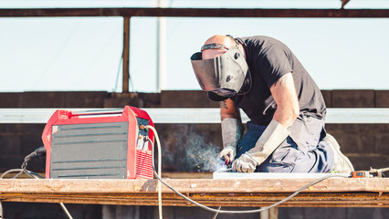 worker on scaffold welding a metal piece with helmet and protective gloves outdoors