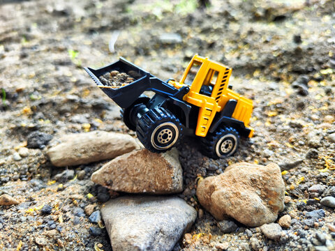 Toy yellow tractor or excavator with a bucket during operation. Road or construction equipment. Loading and unloading work. Building a house or road. Partial focus and blur