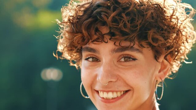 Young beautiful smiling hipster woman in trendy summer clothes. Cute teen model posing in the street background at sunset. Positive brunette female with curls hairstyle. Cheerful and happy 