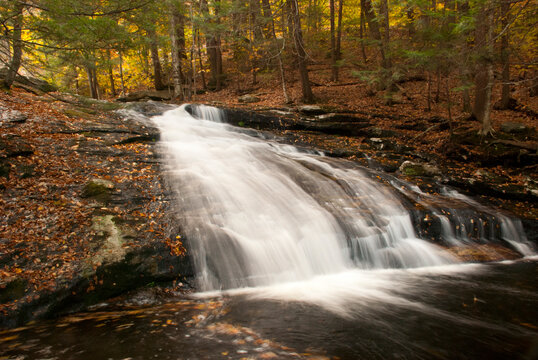 New England waterfalls in autumn. Cascading smooth flowing waterfall with fallen leaves. Waterfall flowing from stream in forest. 