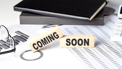 COMING SOON - text on a wooden block with chart and notebook