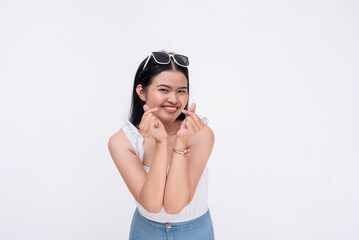 A young lively asian woman does a finger heart gesture while smiling in front of the camera....