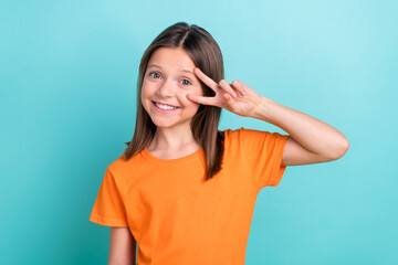 Photo of small funny friendly girl say hi friends showing v sign symbol near eye wear orange...