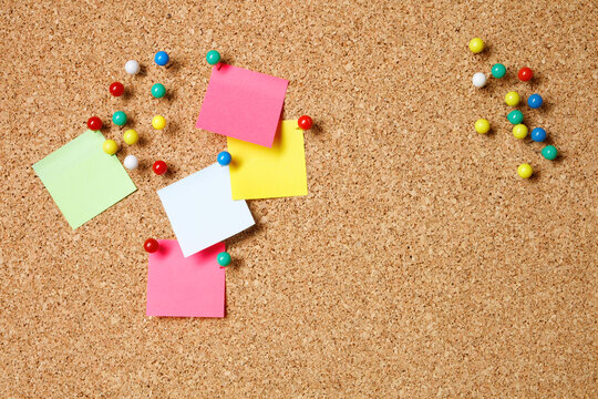Empty colorful notes on cork background. Five sticky notes in various colors with pushpins and blank space on cork background.