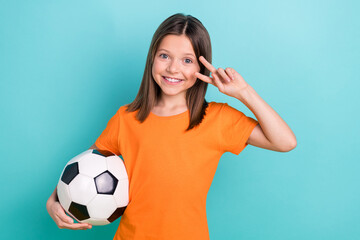 Portrait of cute schoolgirl with straight hair dressed orange clothes hold ball showing v-sign isolated on turquoise color background