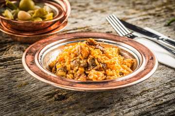 Delicious bulgur pilaf with meat on a bronze plate
wooden background