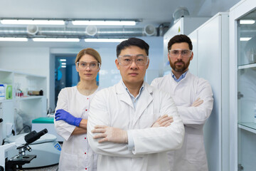 Portrait of a young team of scientists and doctors standing in a modern laboratory in white coats and protective equipment, crossing their arms and seriously looking at the camera.