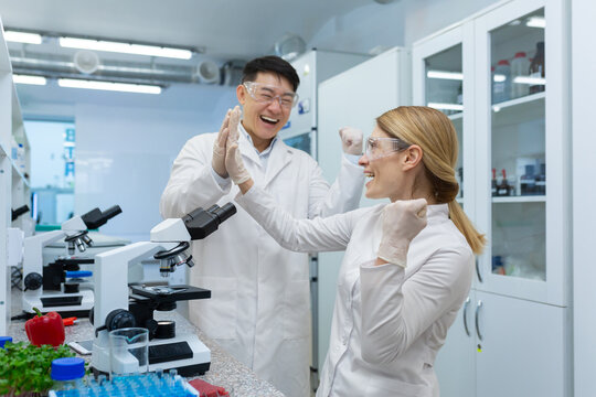A team of scientists, a young Asian man and woman are working in a laboratory with food products. Rejoice in success in research, discovery, congratulate each other.