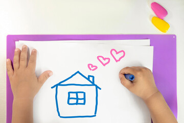 a child draws a house on white paper with crayons, the concept of a family and a cozy home, love...