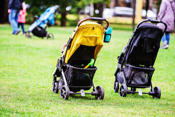 Two baby carriages stand unattended on the lawn in a public place. Foreground