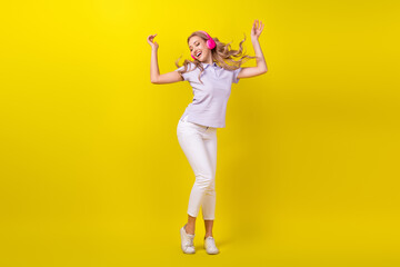 Fototapeta na wymiar Full size photo of satisfied girl wear violet polo white trousers in headphones wind blow on hair isolated on yellow color background
