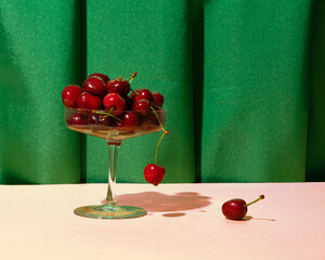 Fresh, ripe cherries in a champagne glass, summer fruit dessert creative serving, deep green satin drapery background. 