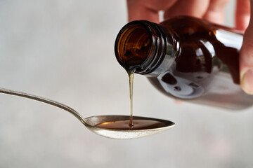 Pouring herbal syrup from a bottle onto a spoon