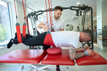 Male performing exercise on suspension trainer supervised by gym instructor